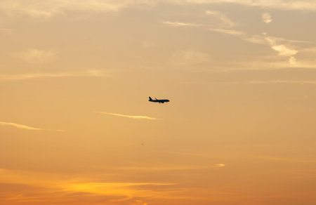 Airplane flying at sunset with orange sky and clouds.