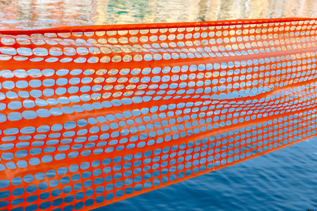 Orange construction barrier with circular openings against blue water.の写真素材
