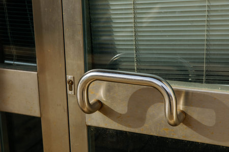 Stainless steel door handle on modern glass door with blinds.