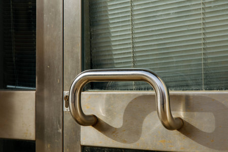 Stainless steel door handle on glass window with horizontal blinds.の写真素材
