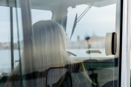 Elderly caucasian woman with gray hair looking out window at waterfront cityscape.の写真素材