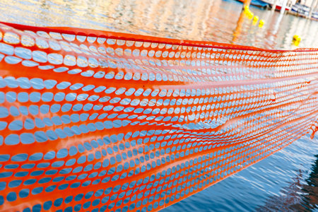 Orange safety netting over water surface with buoys in background.の写真素材