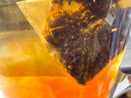 Close-up of herbal tea bag steeping in glass teapot with golden brew.