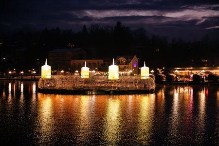Velden, Austria - December 20, 2024: Schlosshotel am Woerthersee shines brightly in winter with large glowing candles on the water, enhancing the festive ambianceの写真素材