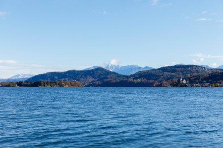 Scenic lake view with distant mountains and autumn colors under clear blue sky.の写真素材