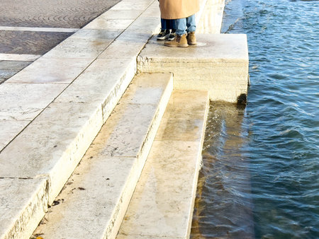 Couple standing on stone steps by river in urban setting.の写真素材