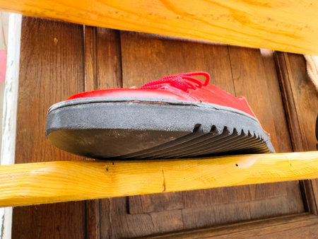 Close-up of red shoe with black sole on wooden shelf.