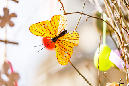 Vibrant orange butterfly resting on branch amidst spring decorations.の写真素材
