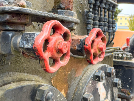 Rusty red valves on weathered industrial equipment in urban setting.