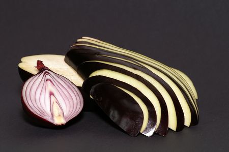 half of onion and sliced eggplant on black paper backgroundの写真素材