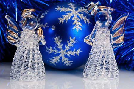 Two decorative glass angel, blue christmas ball and Christmas tree tinsel on white with reflectionsの写真素材