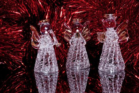 Three decorative christmas angells on black mirror background and some red tinselの写真素材