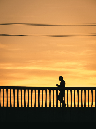 Silhouette of man walking on the bridge with cigarettes on sunset.の写真素材
