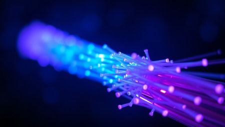 Close-up image of illuminated blue fiber optic cables against a dark, blurred background with bokeh light effects. The glowing fiber ends emphasize the concept of light-based data transmission, representing cutting-edge technology in telecommunications, internet infrastructure, and digital connectivity. Ideal for use in tech-related projects, websites, presentations, and promotional materials focused on innovation, speed, and modern communication systemsの素材