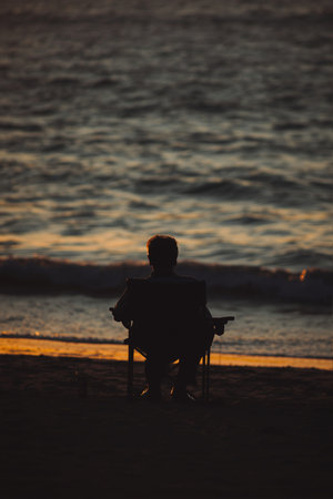 Silhouette of a man sitting on a chair at the beachの素材