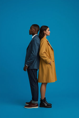 A symmetrical composition of two people in gray and black suits standing upright and facing opposite directions. The solid blue backdrop emphasizes contrast, professionalism, and equality.の素材