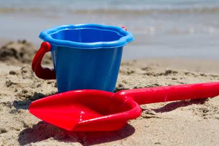 Children's beach toys - red shovel and blue bucket on sand by the sea on a sunny day.の写真素材