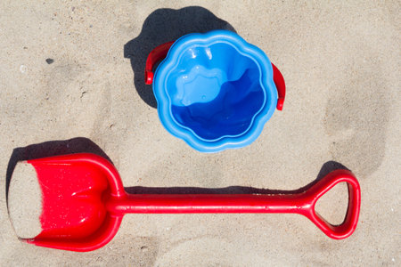 Children's beach toys - red shovel and blue bucket on sand by the sea on a sunny day.の写真素材