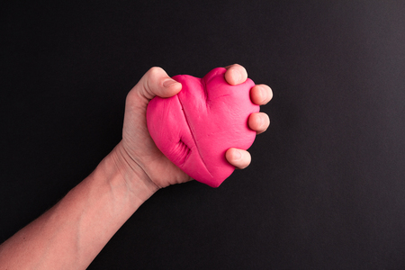 Mens hand squeezing pink scared heart on a black backgroundの写真素材