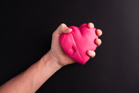 Mens hand squeezing pink scared heart on a black backgroundの写真素材