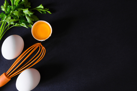 Broken eggs with a whisk . On a black wooden background. Free space for text . Top viewの写真素材