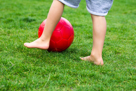 Boy playing football on green grass with red ballの写真素材