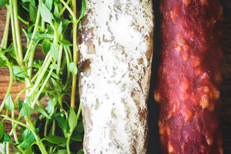 Italian flag made up of red and white salami and green sprigs of thyme on wooden boardの写真素材