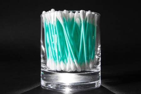 Turquoise cotton swabs in clear glass jar in on black backgroundの写真素材