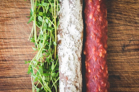 Italian flag made up of red and white salami and green sprigs of thyme on wooden boardの写真素材