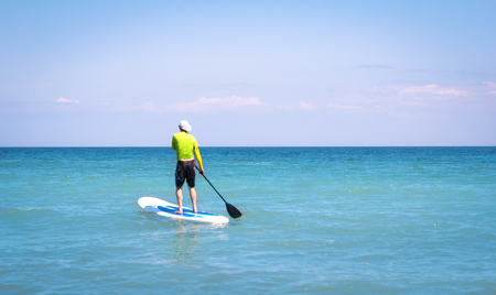 a man on a surfboard floating in the sea with the help of a paddle, Active Beach Lifestyleの写真素材