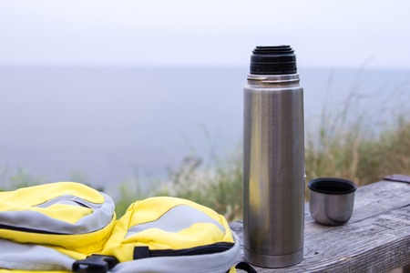 beverage bottle with a cup and a yellow bag on a wooden bench on a background of the seaの写真素材