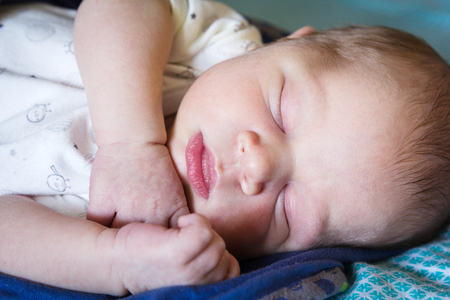 A sweet one month old newborn baby boy is sleeping covered by blanketの写真素材