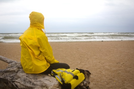 Men in yellow raincoat on the beach looking at storm. Man on the edge of the world conceptの写真素材