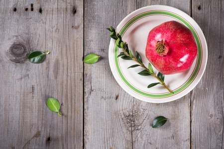 Some whole red pomegranate on the white plate on rustic wooden unpainted grey tableの写真素材