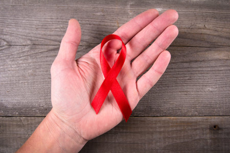 Red ribbon as symbol of aids awareness in men's hand on gray wooden background
