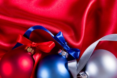 Blue, red and silver christmas balls with ribbons on a red silk clothの写真素材