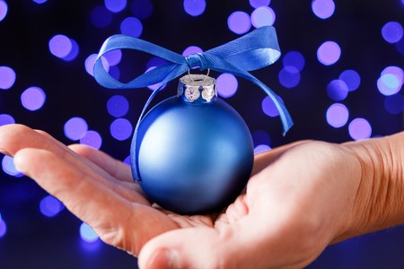 Blue christmas ball in man's palm and blured purple blue and white lights at the backgroundの写真素材
