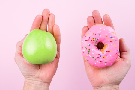 Hands choosing between apple and donut as concept of healty lifestyleの写真素材