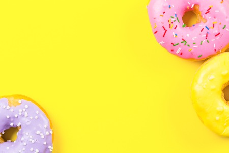 Pink round donut and few other on yellow background. Flat lay, top view.の写真素材
