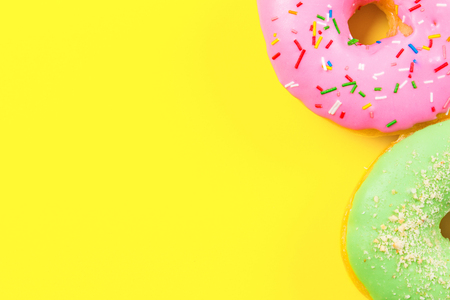 Pink round donut and few other on yellow background. Flat lay, top view.の写真素材