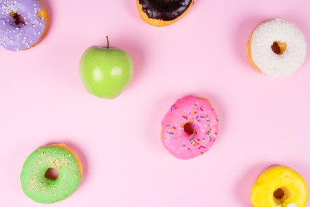 Close-up of tasty donuts and fresh green apple on pink background suggesting healthy food conceptの写真素材