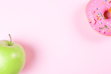 Close-up of tasty donuts and fresh green apple on pink background suggesting healthy food conceptの写真素材