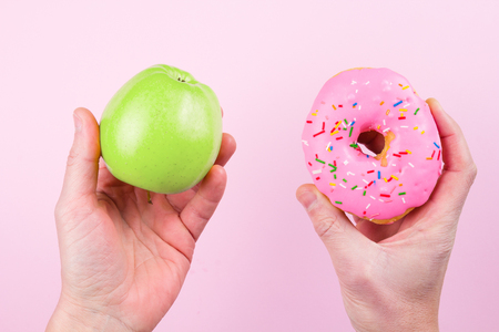 Hands choosing between apple and donut as concept of healty lifestyleの写真素材