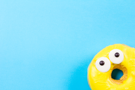 Yellow round donut with eyes on blue background. Flat lay, top view.の写真素材