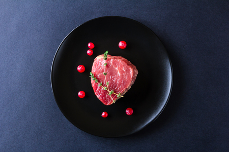 Raw meat herbs and berries on black plate and dark background. Minimalistic still lifeの写真素材