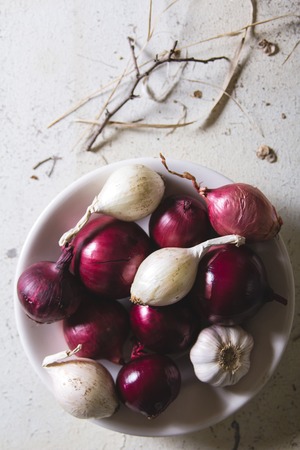 Red and white onion bulbs in the plate an old wooden painted table. Above view still lifeの写真素材