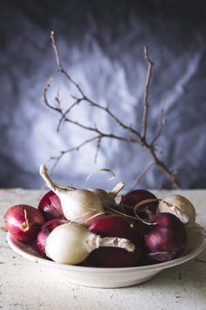 Red and white onion bulbs in the plate an old wooden painted table. Still lifeの写真素材