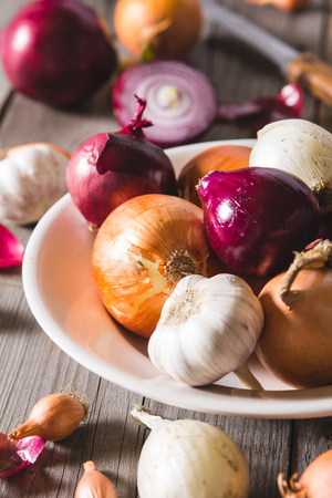 Several kinds of different onion bulbs at a white plate, standing on an old wooden table. Above view still lifeの写真素材