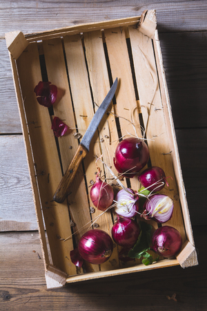 Freshly harvested red onion bulbs in wooden farmers box on old wooden table. Above view still lifeの写真素材