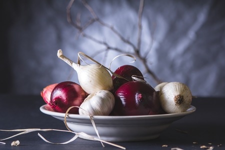 Red and white onion bulbs in the plate on black table. Still lifeの写真素材
